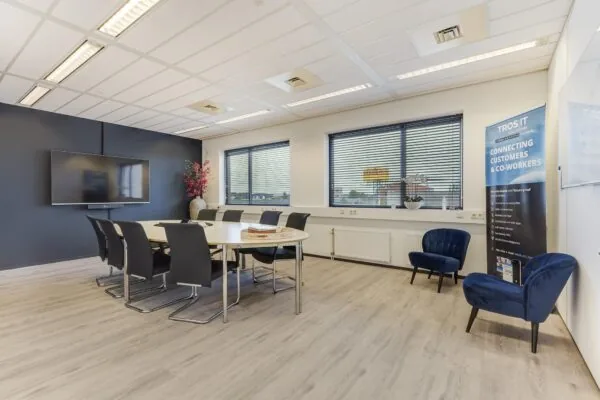 Moderne vergaderruimte aan de Laan van S-Gravenmade met een grote tafel, presentatiescherm en banners van Tros IT.